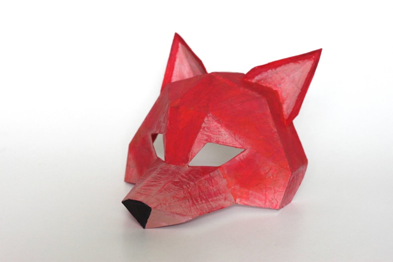 May include: A red paper fox mask with a geometric design. The mask has cut-out eye holes and a pointed nose.