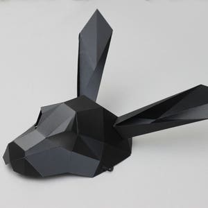 Puede incluir: Una m&aacute;scara de papel negra con forma de cabeza de conejo con caracter&iacute;sticas geom&eacute;tricas.