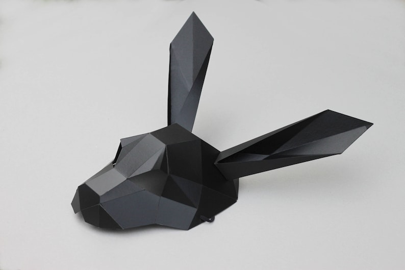 Puede incluir: Una m&aacute;scara de papel negra con forma de cabeza de conejo con caracter&iacute;sticas geom&eacute;tricas.