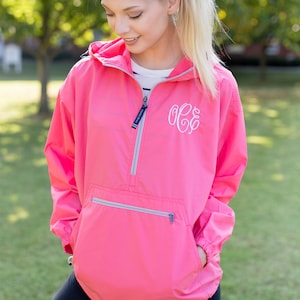 May include: A pink hooded jacket with a zipper and a white monogram on the front. The jacket has a kangaroo pocket and a drawstring hood.
