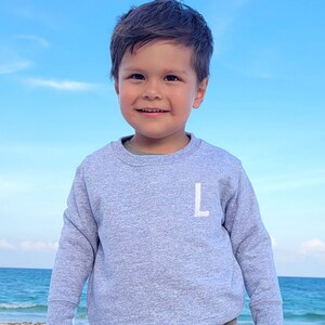 little boy on a beach wearing a gray crewneck with single intial embroidered design