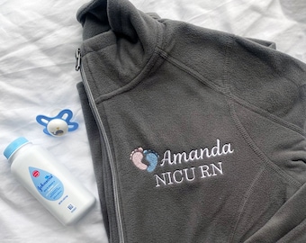 May include: Gray fleece jacket with a zipper and a white embroidered design of two baby footprints and the text "Amanda NICU RN".