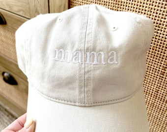 May include: A beige baseball cap with white embroidery that reads "mama".