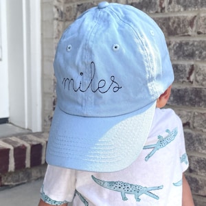 May include: A light blue baseball cap with the name "Miles" embroidered in black thread.