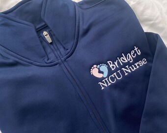 May include: A navy blue zippered jacket with a white embroidered design of two footprints inside a heart and the text "Bridget NICU Nurse".
