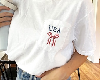 USA-randig rosettbroderad t-shirt med fickor i bekväma färger | Coquette 4 juli-topp | Söt USA-t-shirt | Trendig rosett | Patriotisk rosett | CC30EFJ1