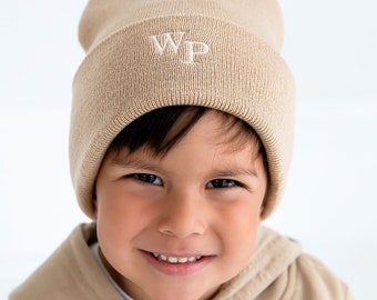 May include: A young person wearing a beige knitted beanie with the letters "WP" embroidered on the front. The beanie is folded down over their forehead.