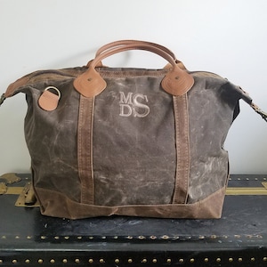 May include: A brown canvas and leather duffel bag with a monogrammed "MDS" on the front. The bag has a brown leather handle and a zipper closure.