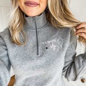 May include: Gray sweatshirt with a white embroidered design that says "Kaitlyn RN" with a stethoscope and a heartbeat graphic.