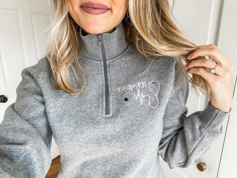 May include: Gray sweatshirt with a white embroidered design that says "Kaitlyn RN" with a stethoscope and a heartbeat graphic.