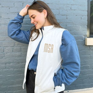 May include: A white vest with a zipper closure and two pockets. The vest has the letters "MSA" embroidered on the front in gold thread.