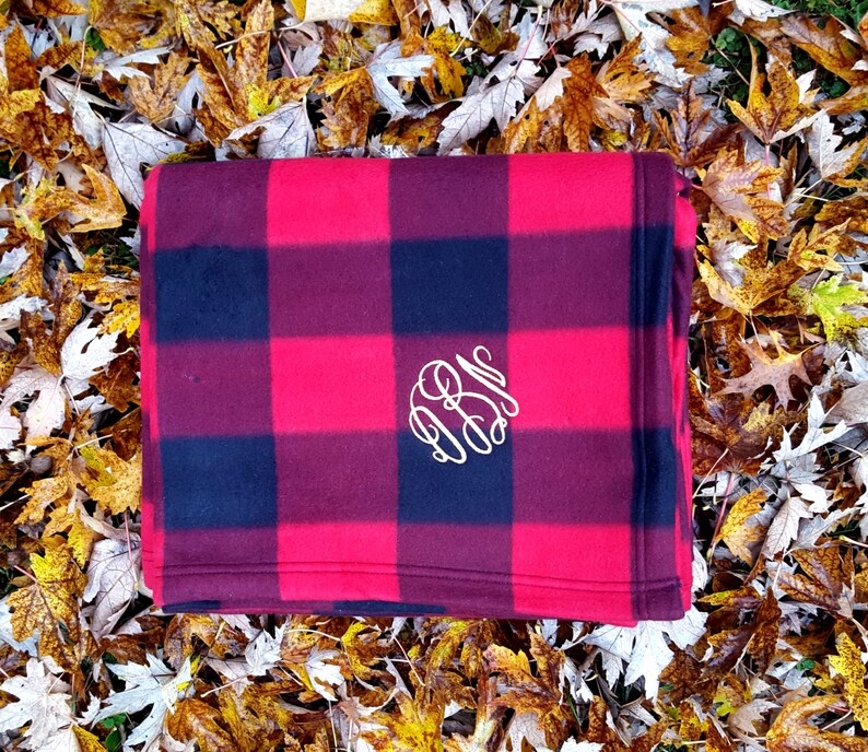 May include: A red and black buffalo plaid fleece throw blanket with a white monogram in the center.