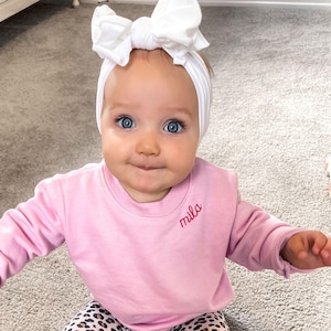 toddler girl wearing a pink crewneck sweatshirt with embroidered name along the collar