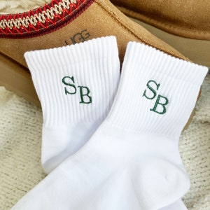 May include: A pair of white ankle socks with green embroidered initials "SB" on each sock.
