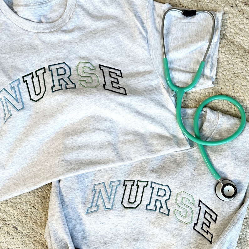 an ash crewneck sweatshirt and t-shirt with custom NURSE embroidered design in shades of blue and green