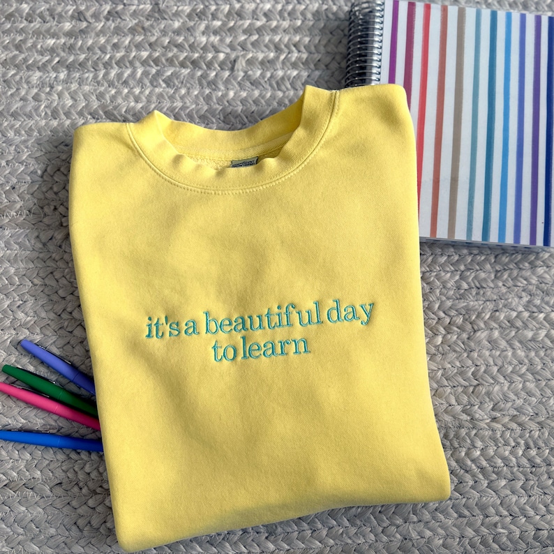 Puede incluir: Sudadera amarilla con el texto "it's a beautiful day to learn" bordado en verde.
