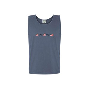A blue jean comfort colors tank top with embroidered mini usa flags and dainty bow design across the chest in an alternating pattern