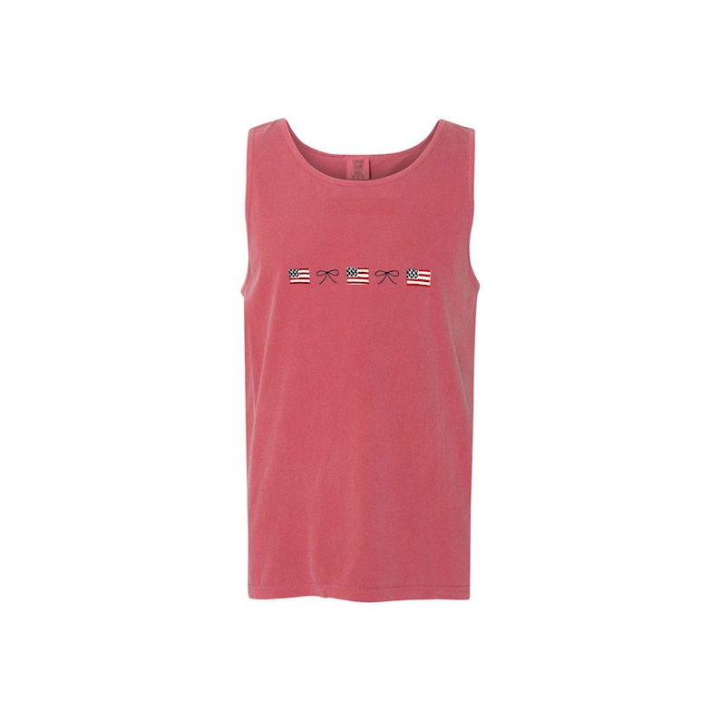 A crimson comfort colors tank top with embroidered mini usa flags and dainty bow design across the chest in an alternating pattern