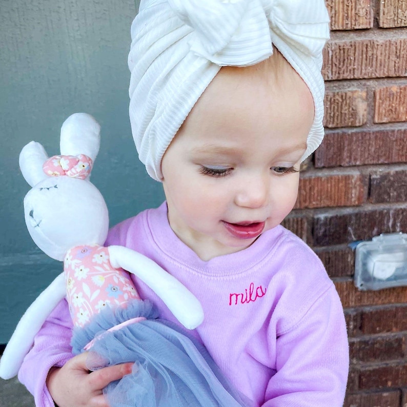 toddler girl wearing a pink crewneck sweatshirt with embroidered name along the collar