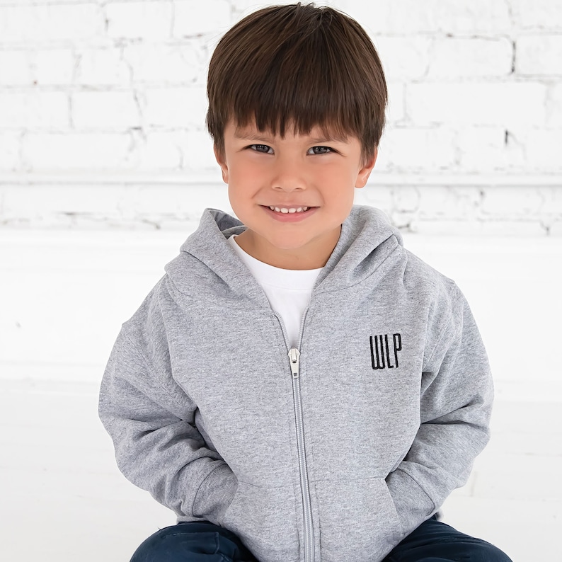 toddler boy wearing a full zip hooded heather grey sweatshirt with embroidered monogram on the left chest