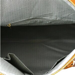 May include: An open brown tote bag with a black and white herringbone pattern lining. The bag features a zippered top and several internal pockets. The zip pull is gold-coloured.