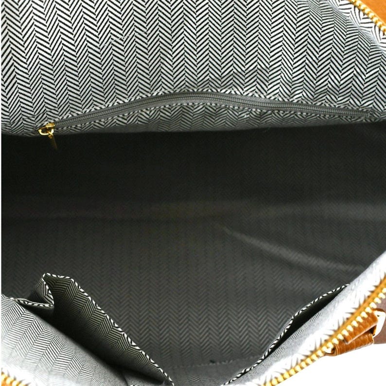 May include: An open brown tote bag with a black and white herringbone pattern lining. The bag features a zippered top and several internal pockets. The zip pull is gold-coloured.