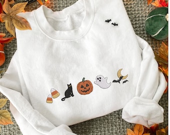 Puede incluir: Sudadera blanca con diseños bordados de temática Halloween. El diseño incluye caramelos de maíz, un gato negro, una calabaza, un fantasma, una luna creciente y murciélagos. Prenda cómoda e informal.