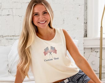 May include: Cream-colored tank top with embroidered American flags and the text "Custom Text". The top is paired with black and white checkered shorts. The outfit is casual and comfortable.