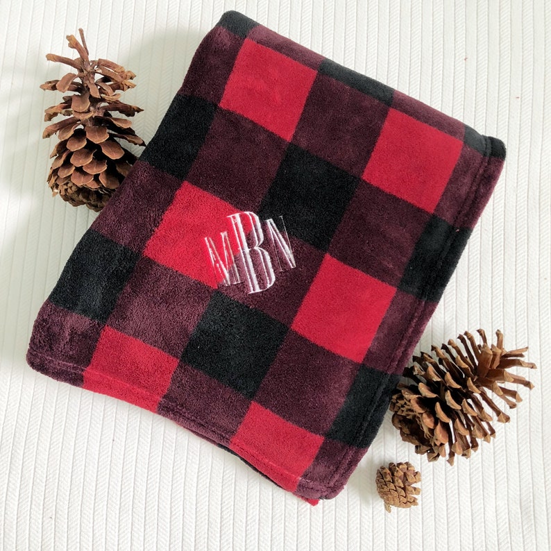 May include: A red and black plaid fleece throw blanket with the monogram "MBM" embroidered in white.