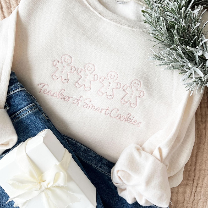 sweet cream crewneck sweatshirt with custom gingerbread men icons and "teacher of smart cookies" design embroidered in powder pink thread
