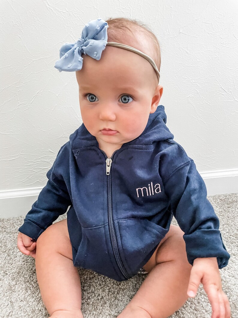 baby girl wearing a full zip hooded navy sweatshirt with embroidered name on the left chest