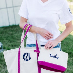 Pode incluir: Uma bolsa tote de lona branca com acabamento rosa e um monograma azul marinho "EZL" na frente. Uma bolsa de lona branca menor com acabamento rosa e o nome "Emily" bordado em azul marinho est&aacute; presa &agrave; bolsa tote.