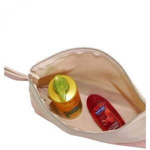 Pode incluir: Uma bolsa de viagem com z&iacute;per rosa e bege com um puxador de z&iacute;per. A bolsa est&aacute; aberta e cont&eacute;m uma garrafa amarela de protetor solar e uma garrafa vermelha de sabonete l&iacute;quido. A garrafa de sabonete l&iacute;quido tem o texto "Softsoap" impresso.