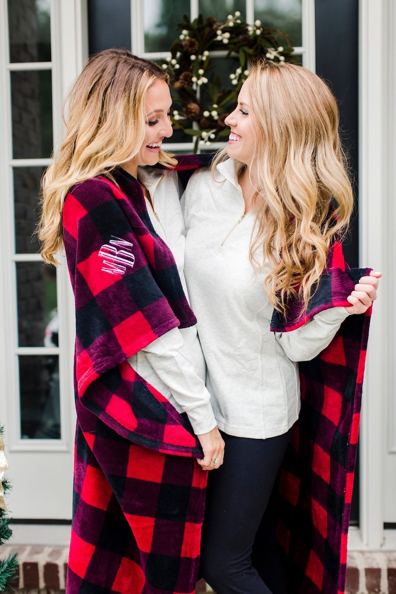 May include: Two people wearing white shirts and black pants are standing next to each other. One person is wearing a red and black plaid blanket. The blanket has the initials "MRN" embroidered on it.