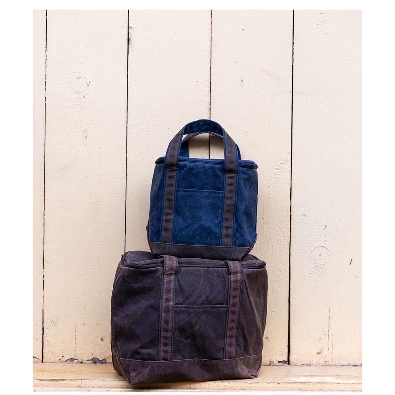 May include: Two canvas tote bags stacked on top of each other. The top bag is dark blue with black straps and the bottom bag is brown with black straps.
