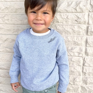 toddler boy wearing a heather grey crewneck sweatshirt with embroidered name along the collar