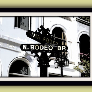 May include: A black and gold street sign with the text "Via Rodeo" and "N. Rodeo Dr." on a white building with arched doorways.