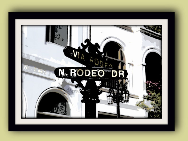May include: A black and gold street sign with the text "Via Rodeo" and "N. Rodeo Dr." on a white building with arched doorways.