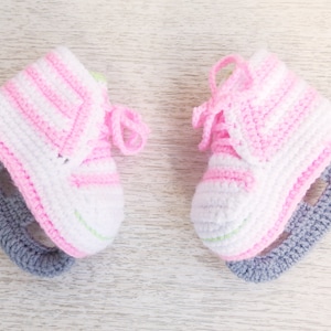 May include: A pair of pink and white crocheted baby booties with gray crocheted skate blades.