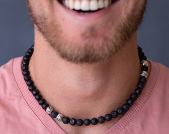 May include: A black lava rock beaded necklace with silver accents. The necklace is worn by a person with a pink shirt.