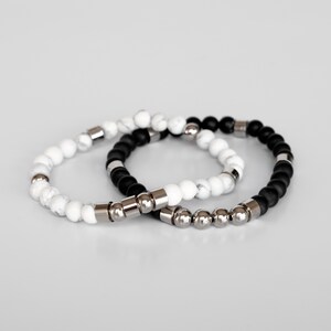 May include: Two beaded bracelets, one black and one white, with silver metal accents.