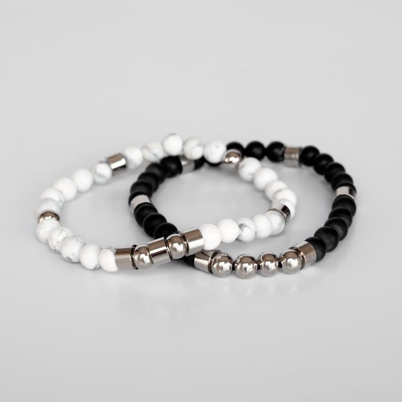 May include: Two beaded bracelets, one black and one white, with silver metal accents.