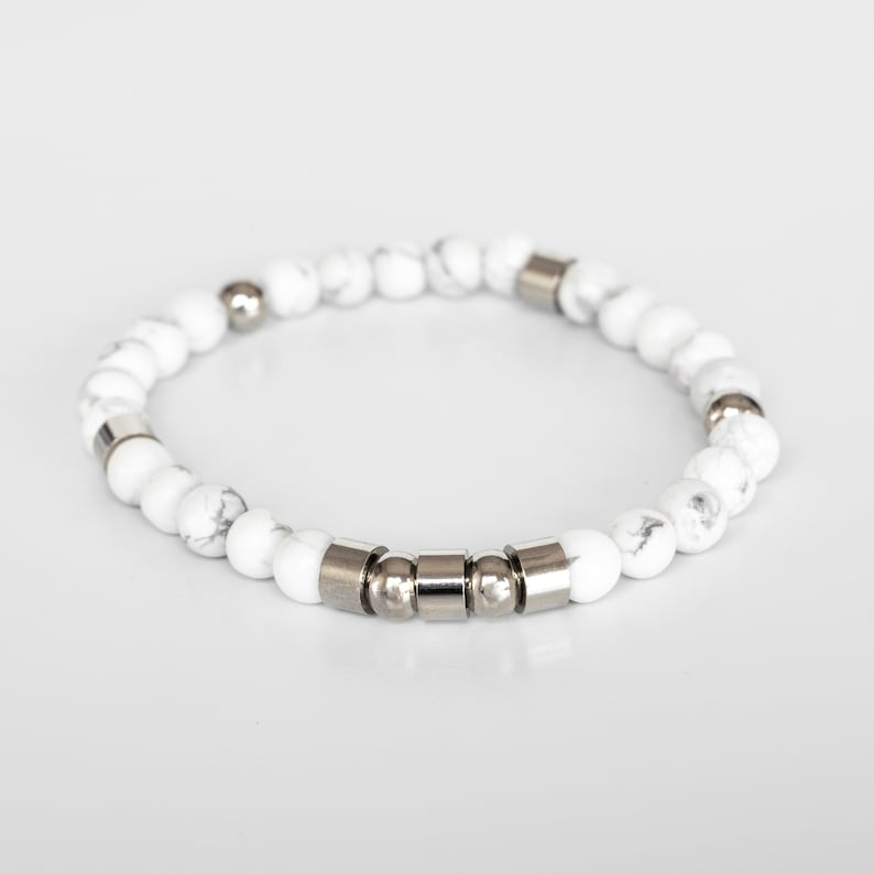 May include: White gemstone bracelet with silver metal accents. The bracelet is made of small, round beads and has a simple, elegant design.