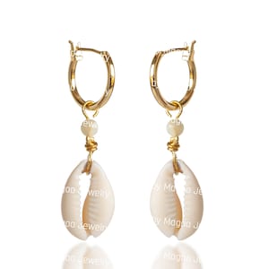 May include: Gold hoop earrings with a white cowrie shell charm and a small gold bead. The earrings are hanging from the hoops.