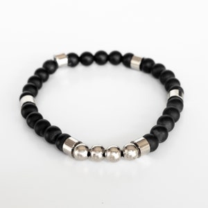 May include: A black beaded bracelet with silver accents. The bracelet has a row of silver beads in the center.