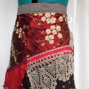 Puede incluir: Una falda de varias capas con una cintura marrón, tela floral roja y dorada, un ribete de encaje rojo y dorado y un ribete de ganchillo marrón y blanco.