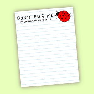 May include: A white notepad with blue lines, featuring the handwritten text "DON'T BUG ME I'M WORKING ON MY TO DO LIST". A cartoon ladybird with a red body and black spots is drawn on the top right.