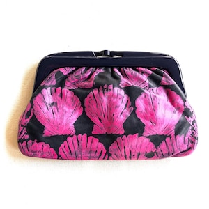 May include: A black clutch purse with a pink seashell pattern. The purse has a metal clasp closure.