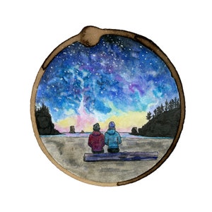 May include: A watercolor painting of two people sitting on a log, looking out at a beach scene with a starry sky and a colorful sunset. The painting is framed in a circle.