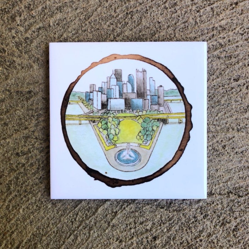 Pode incluir: Uma ilustra&ccedil;&atilde;o em aquarela de um horizonte da cidade com um parque e uma fonte em primeiro plano. A ilustra&ccedil;&atilde;o &eacute; emoldurada por um c&iacute;rculo marrom que se assemelha a um anel de &aacute;rvore.